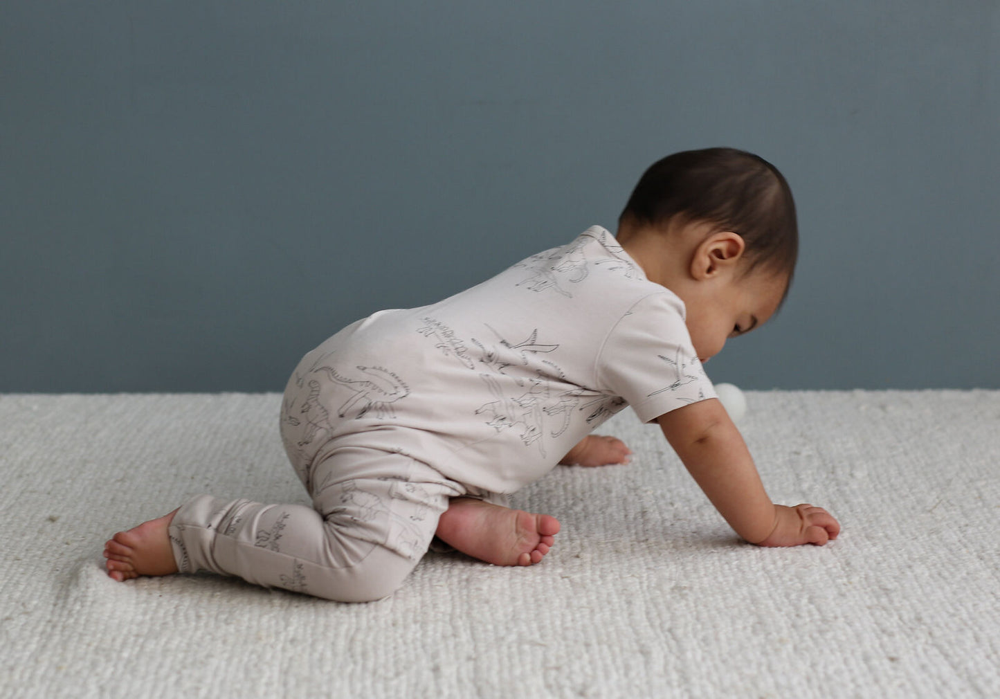 Baby in a light-colored onesie crawling on a textured surface with a neutral background