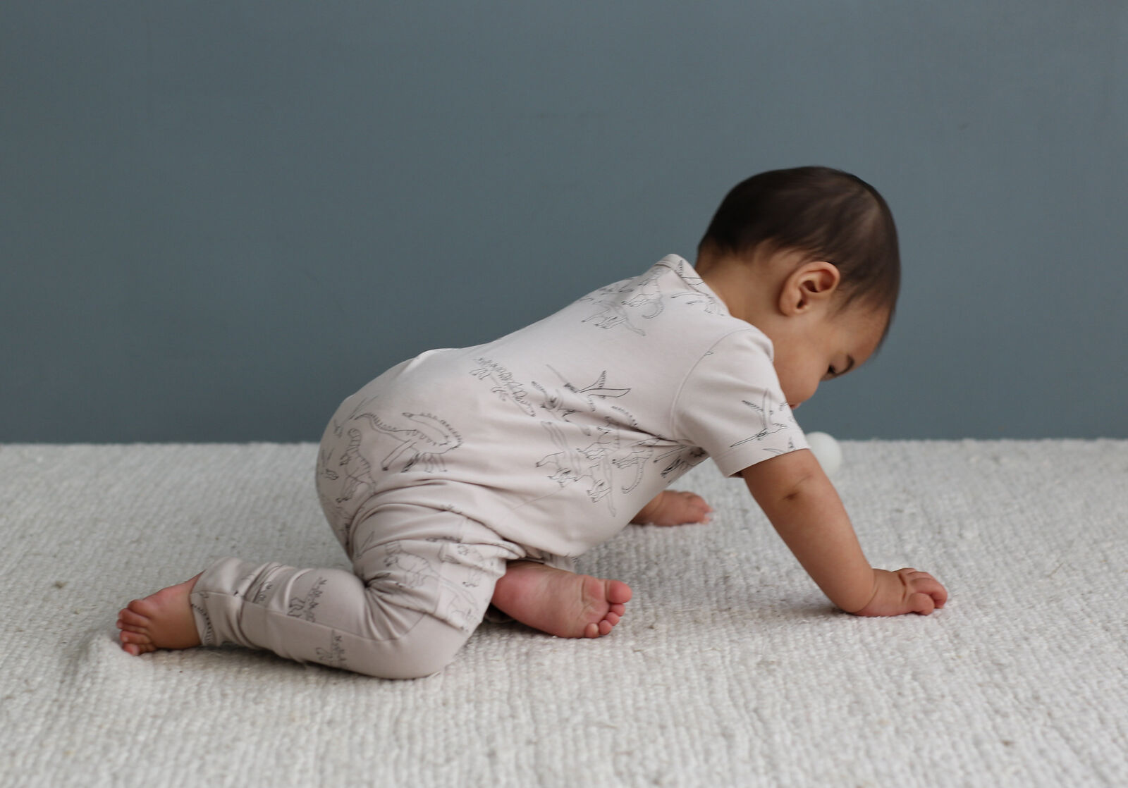 Baby in a light-colored onesie crawling on a textured surface with a neutral background