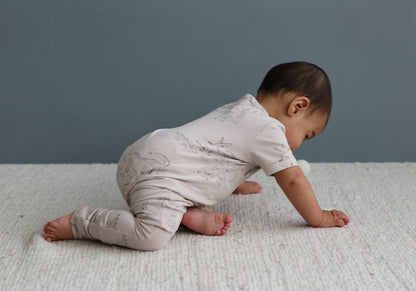 Baby in a light-colored onesie crawling on a textured surface with a neutral background