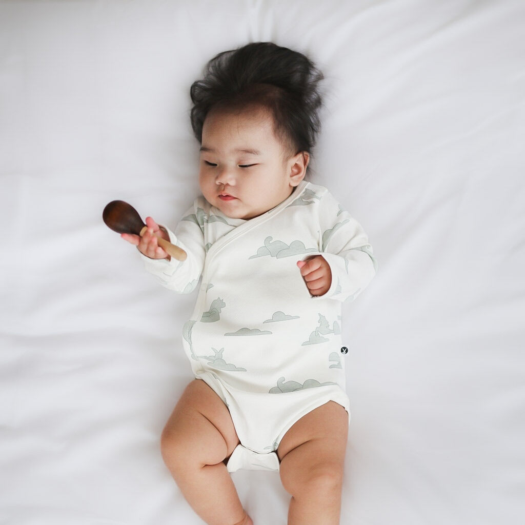 Baby in a white onesie with cloud pattern holding a wooden spoon on a white background