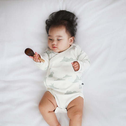 Baby in a white onesie with cloud pattern holding a wooden spoon on a white background