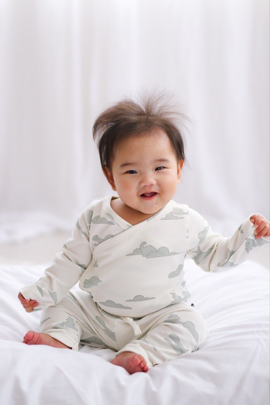 Baby wearing a white outfit with gray cloud patterns on a white background