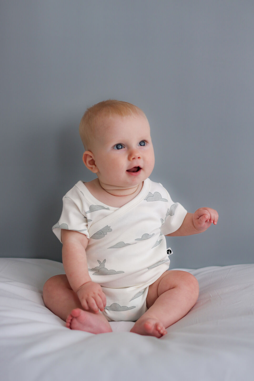 Baby sitting on a white surface with a gray background