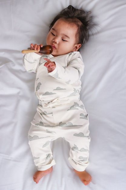 Baby in a white onesie with cloud pattern lying on a white surface