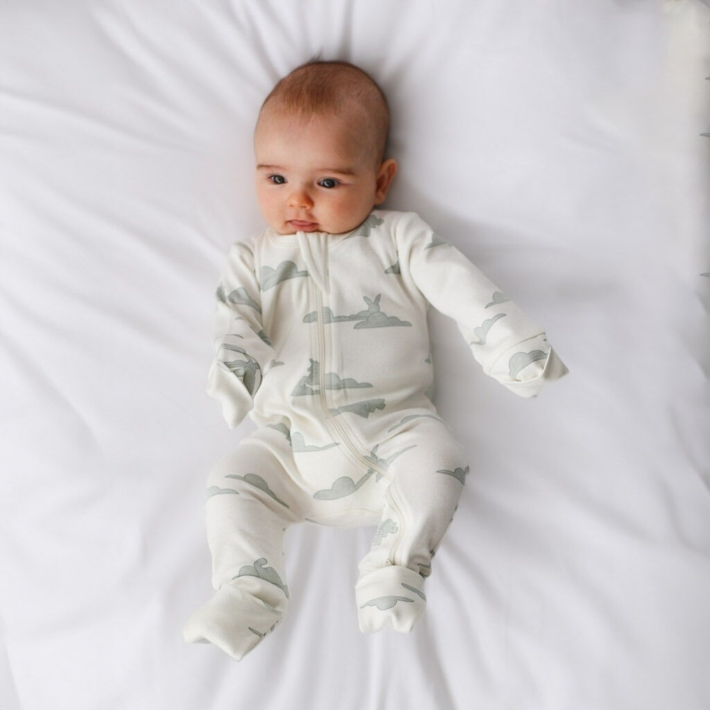 Baby wearing a white onesie with gray airplane patterns on a white blanket
