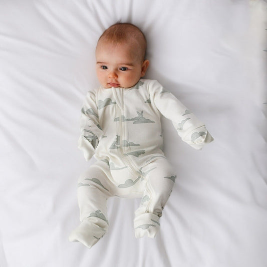 Baby wearing a white onesie with gray airplane patterns on a white blanket
