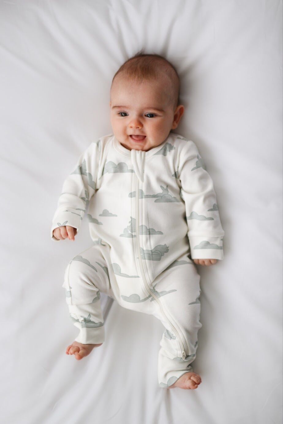 Baby wearing a white onesie with cloud pattern on a white background