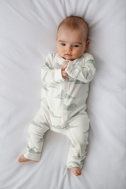 Baby wearing a white onesie with green cloud pattern on a white blanket
