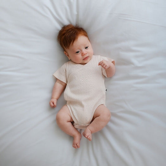 Baby in a beige onesie lying on a white bed