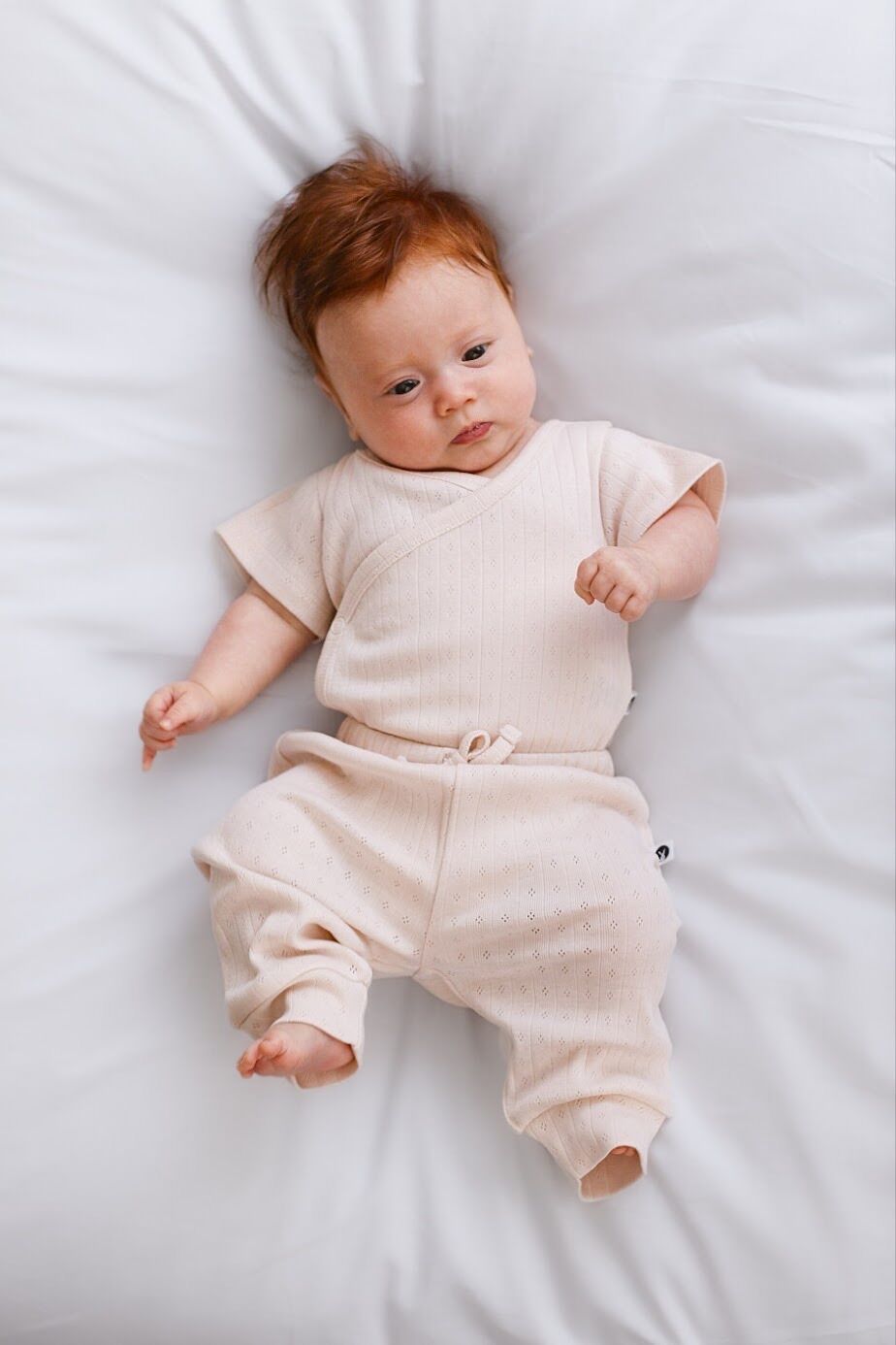 Baby wearing a beige onesie lying on a white surface