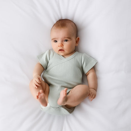 Baby wearing a light green onesie lying on a white surface