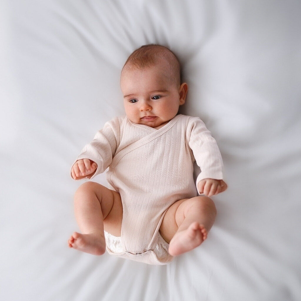Baby wearing a white onesie lying on a white surface
