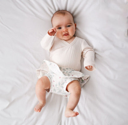 Baby lying on a white bed wearing a white outfit with a patterned diaper.