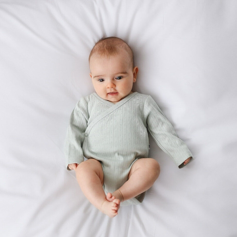 Baby wearing a light green onesie on a white background
