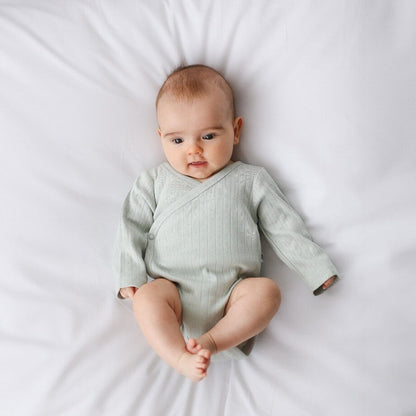 Baby wearing a light green onesie on a white background