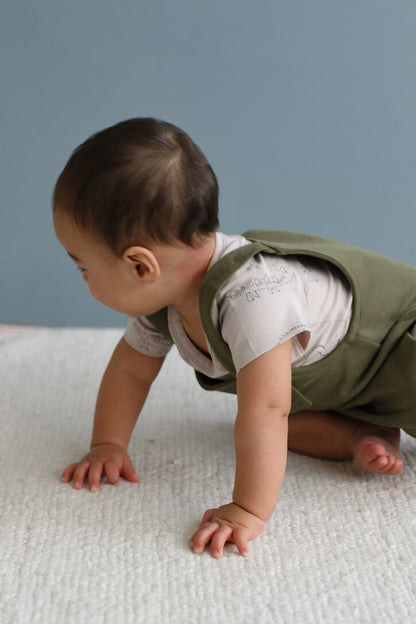 Baby in a green vest crawling on a textured surface with a gray background