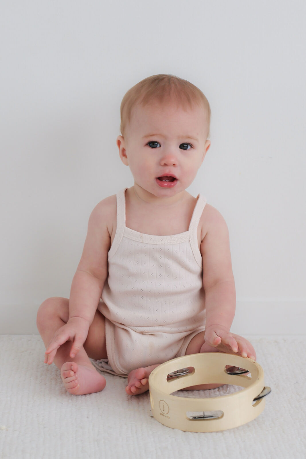 Baby sitting on a white blanket with a tambourine