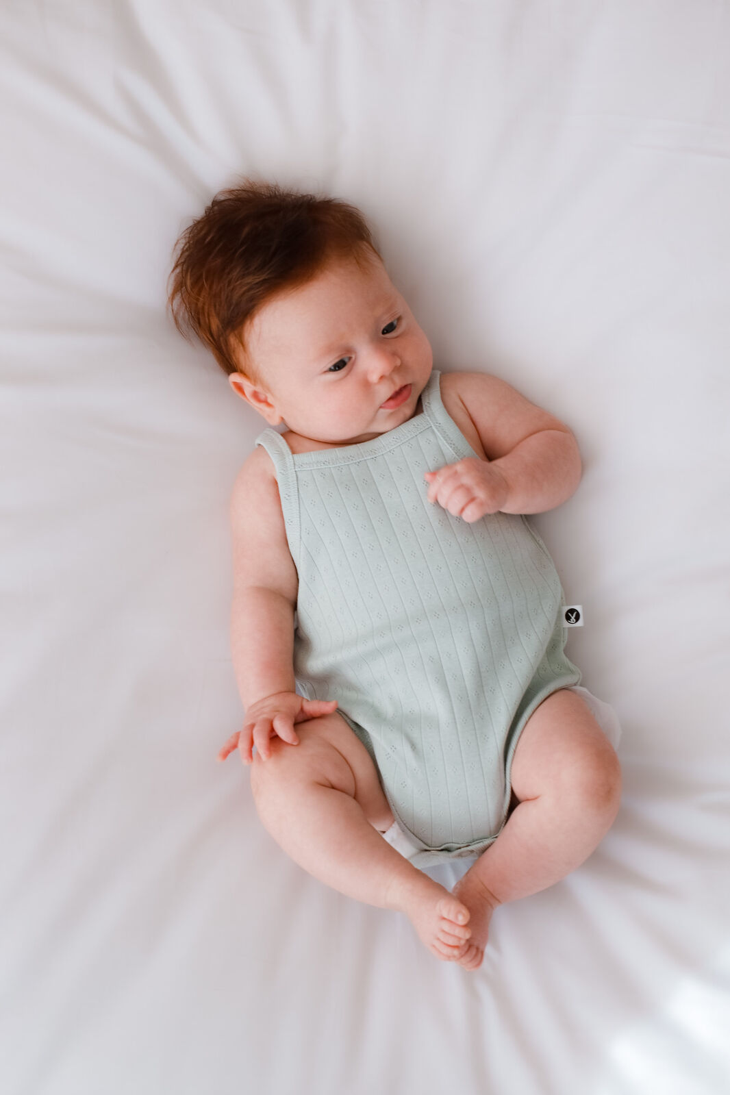 Baby wearing a light green sleeveless romper lying on a white surface