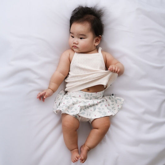 Baby lying on a white bed wearing a white top and patterned shorts.