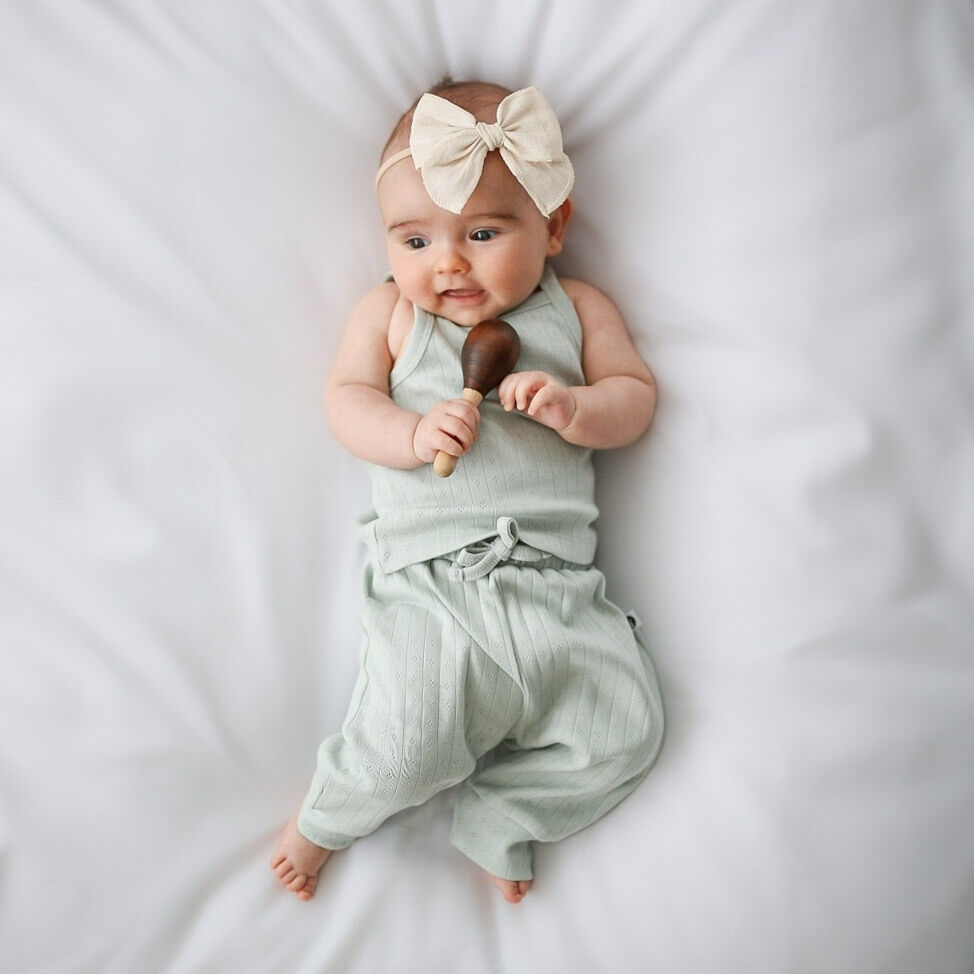 Baby in a light green outfit with a bow headband holding a toy on a white background