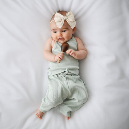Baby in a light green outfit with a bow headband holding a toy on a white background