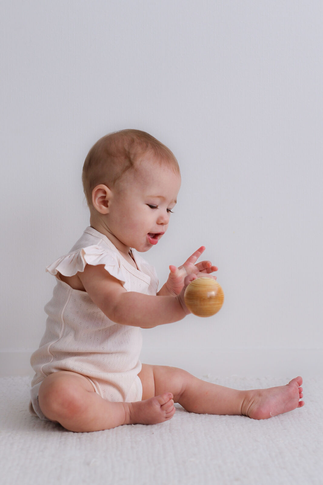 Baby in a white onesie playing with a wooden ball on a light background