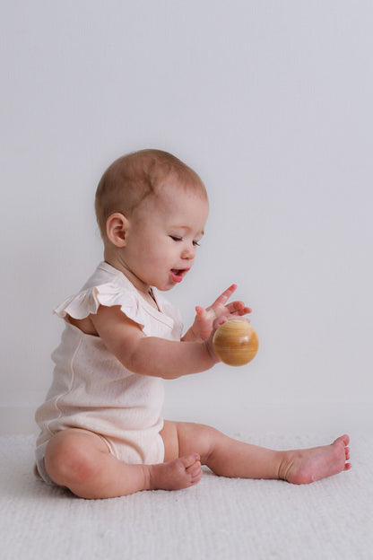 Baby in a white onesie playing with a wooden ball on a light background