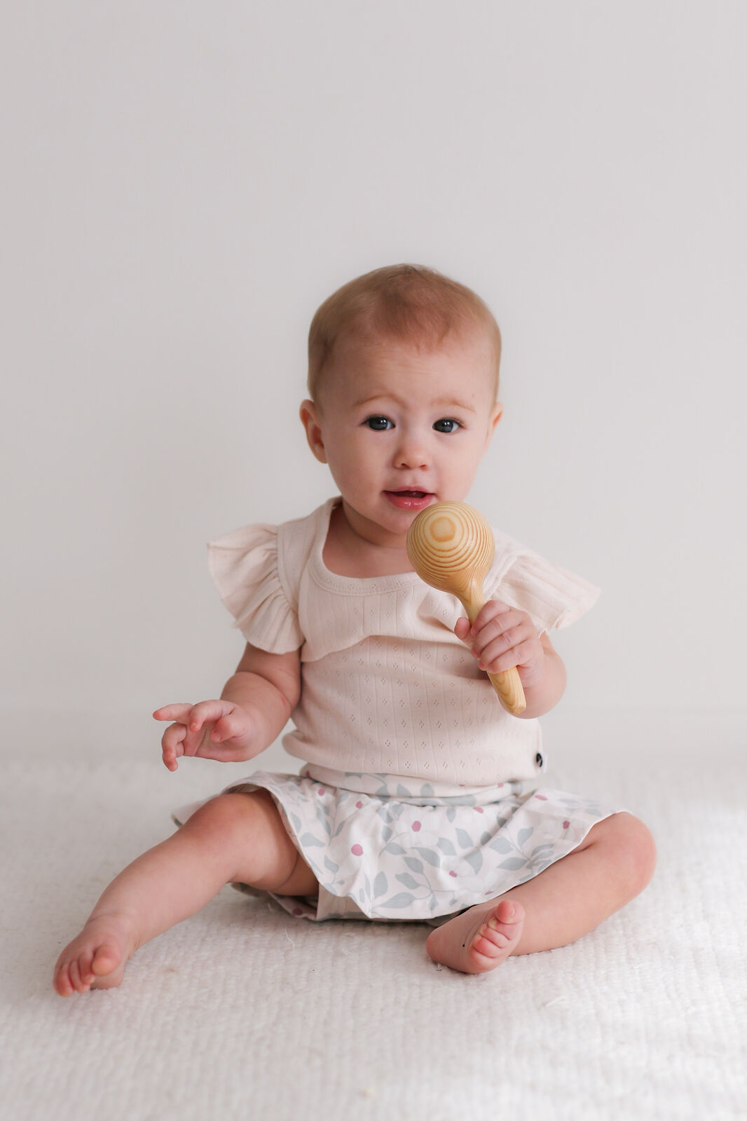 Baby holding a wooden rattle against a plain background