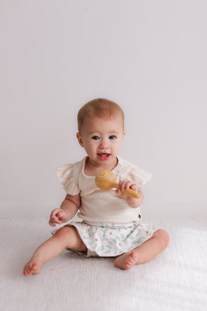 Baby sitting on a white surface holding a wooden toy