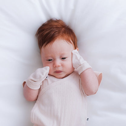 Baby lying on a white surface wearing a light-colored outfit.