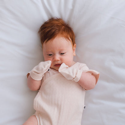 Baby wearing a beige onesie lying on a white surface