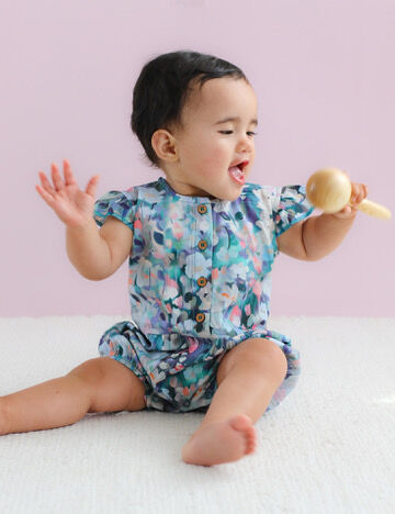 Baby in a floral romper sitting on a white surface with a pink background