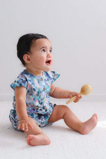 Baby in a floral onesie holding a wooden spoon on a white background