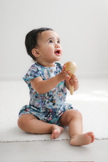 Baby in a floral onesie holding a wooden toy on a white background