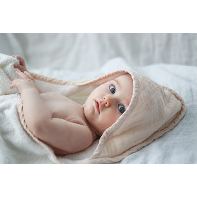 Baby lying down and wrapped in Blush Essential Baby Hooded Towel designed by Burrow and Be