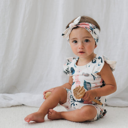 Girl sitting on the carpet in front of white curtains and wearing Pink Clementine Headband, Flutter Bodysuit and Bike Shorts, all designed by Burrow and Be