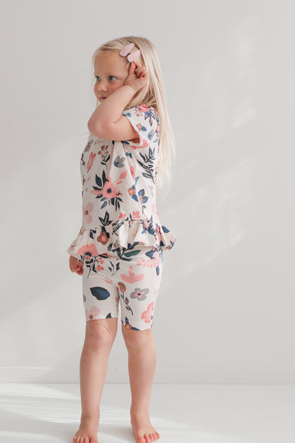 Girl posing in front of a white wall while wearing Pink Clementine Hana Top and Bike Shorts, both designed by Burrow and Be