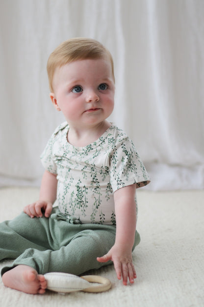 Baby siting on carpet in front of a white curtain while wearing Pointelle Baby Pants in Sage and String of Pearls Short Sleeve Bodysuit, designed by Burrow and Be