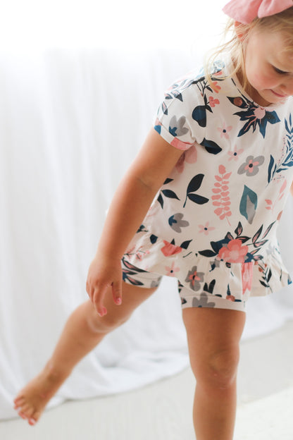 Girl standing in front of a white curtain while wearing Blush Bow Tie Hair Clip, Pink Clementine Hana Top and Bike Shorts, all designed by Burrow and Be