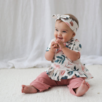 Baby sitting on a carpet in front of a white curtain while wearing Pink Clementine Headband, Hana Top and Pointelle Long Pants in Dusk, all designed by Burrow and Be
