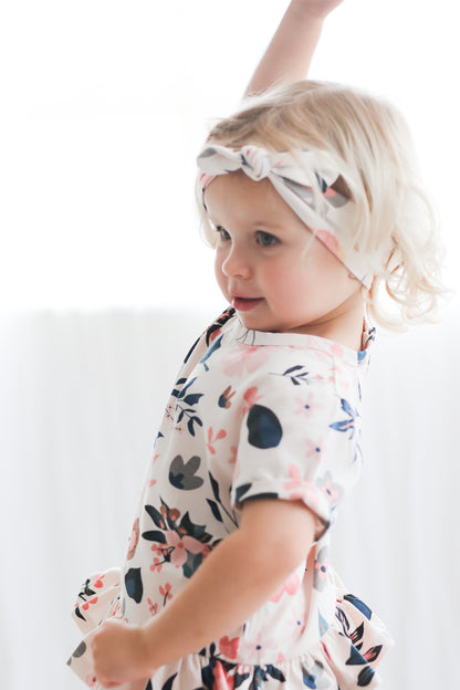 Girl standing in front of a white curtain while wearing Pink Clementine Headband and Hana Top, all designed by Burrow and Be
