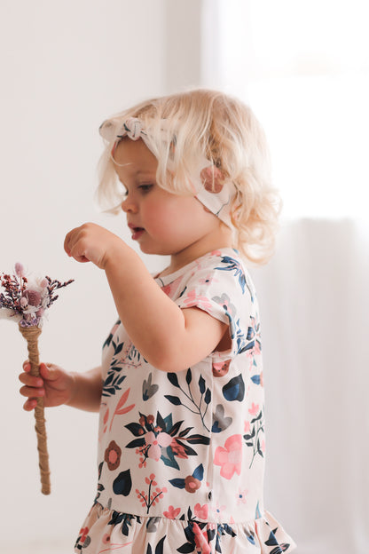 Girl standing in front of a white curtain while wearing Pink Clementine Headband and Hana Top, all designed by Burrow and Be