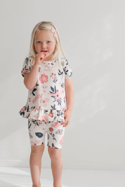 Girl standing in front of a white wall while wearing Pink Clementine Hana Top and Bike Shorts, all designed by Burrow and Be