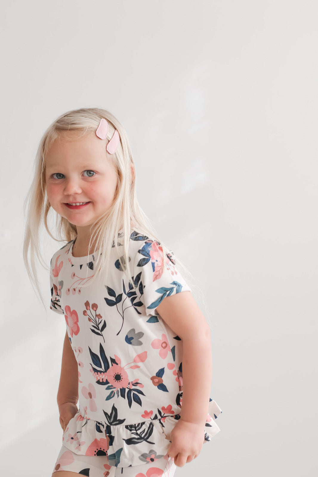 Girl standing in front of a white wall while wearing Pink Clementine Hana Top and Bike Shorts, all designed by Burrow and Be