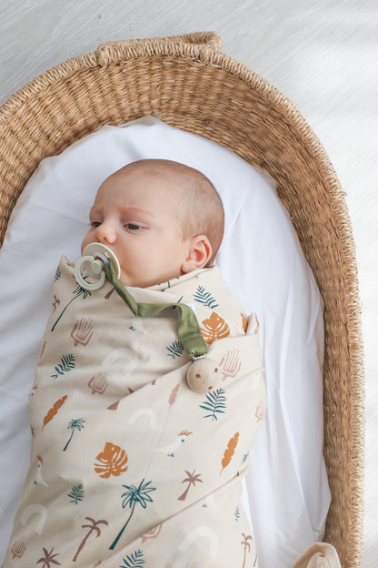 Baby laying in Moses Basket with white sheets, wrapped in Jungle Stamp Stretchy Swaddle, designed by Burrow and Be