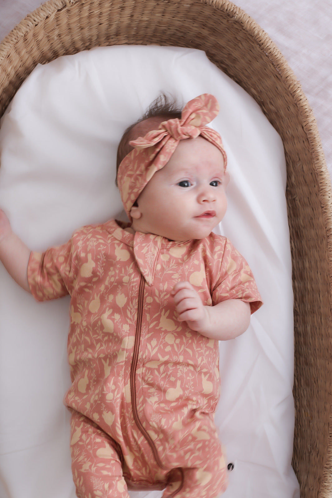 Baby in moses basket wearing Burrow and Be Mead-Doe Zip Suit and Headband