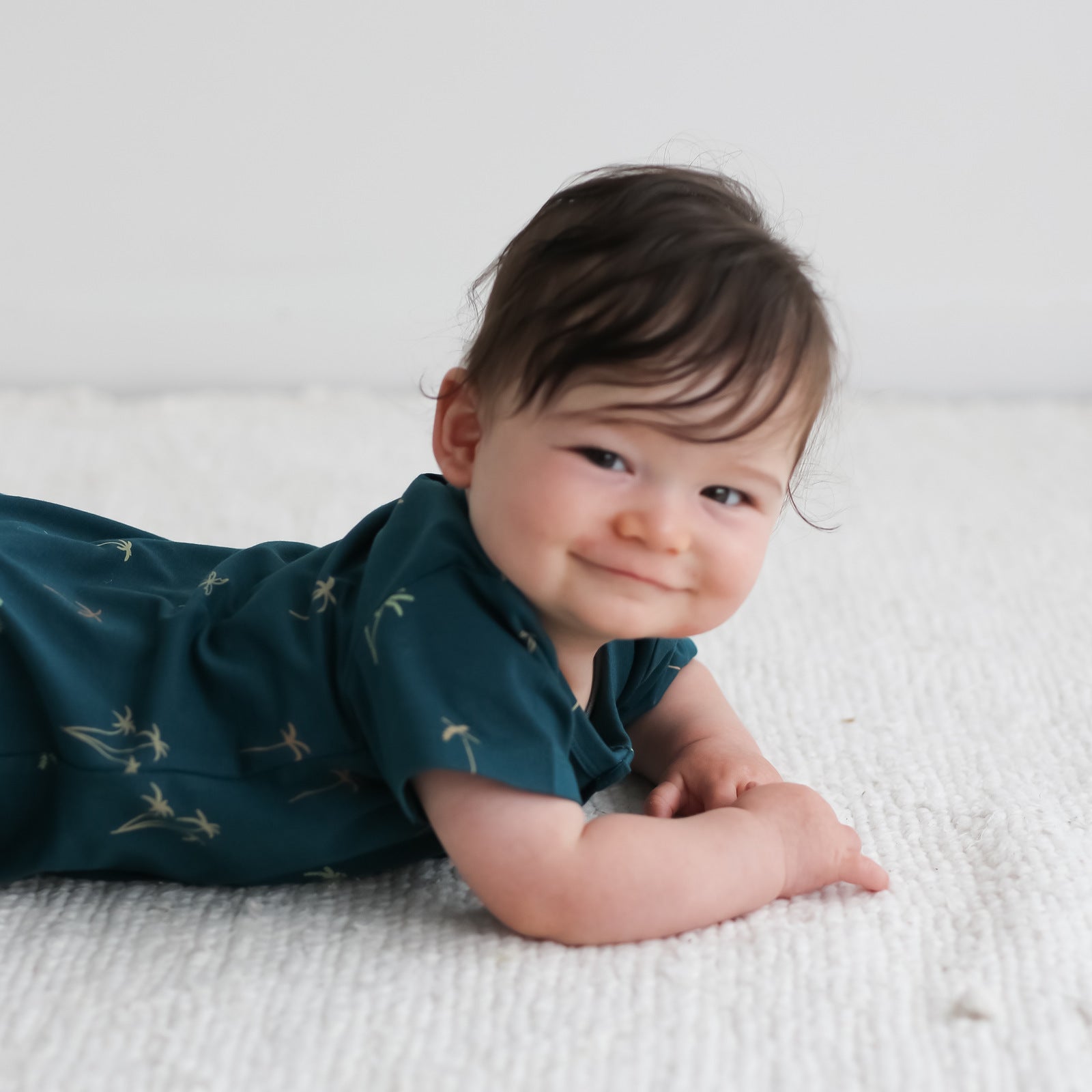 Baby lying on the floor smiling while wearing Palm Alex Romper from Burrow and Be
