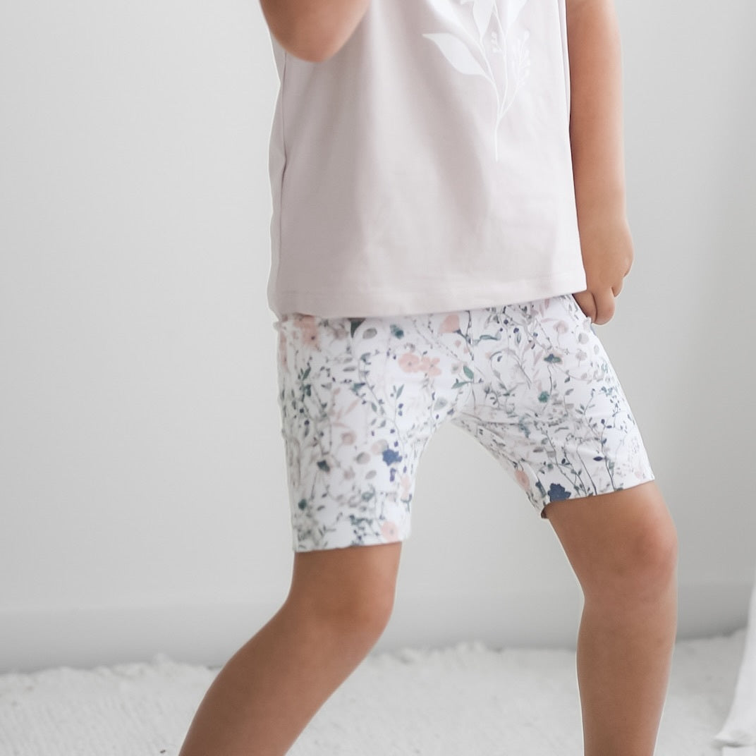 Girl standing in front of white background, wearing Wildflower/Lavender Flutter T-Shirt and Wildflower Bike Shorts, both designed by Burrow and Be