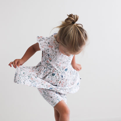Girl standing in front of white background, wearing Wildflower Flutter Dress and Wildflower Bike Shorts, both designed by Burrow and Be