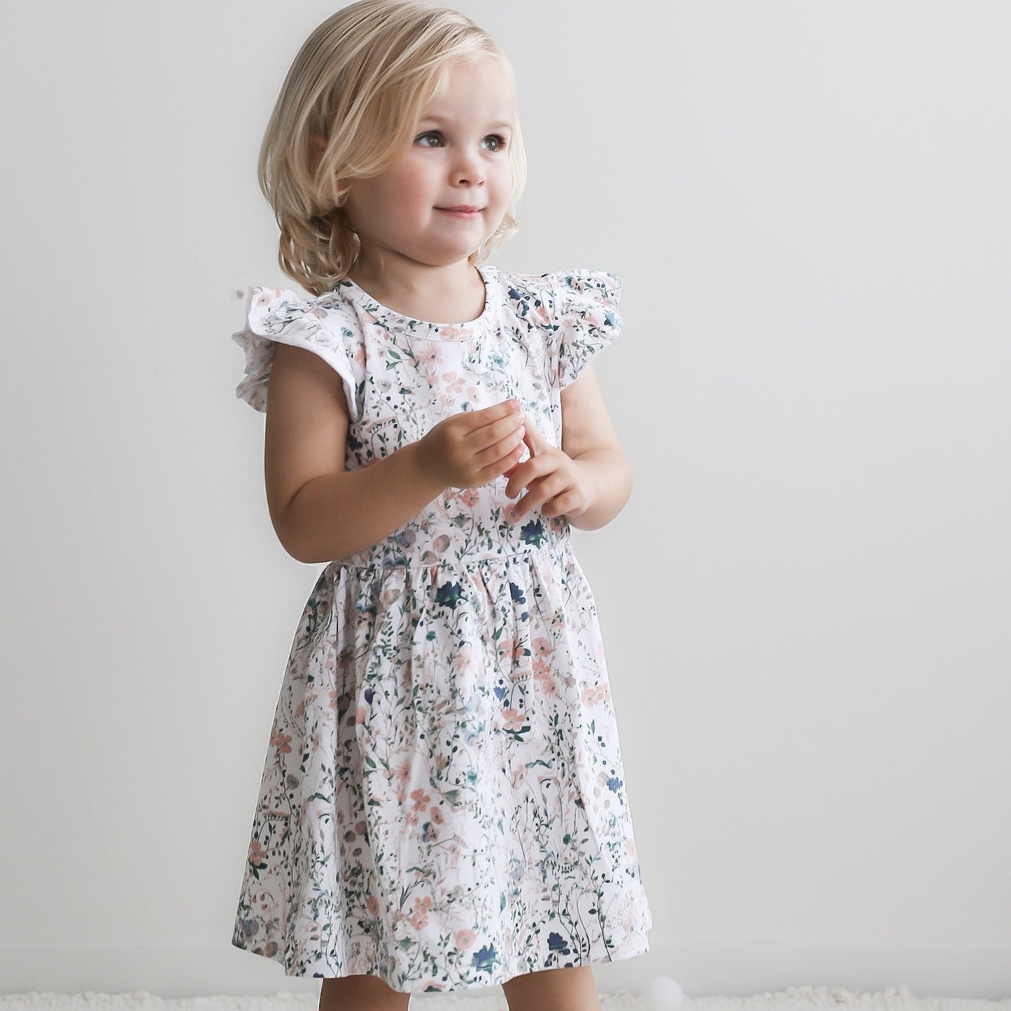 Girl standing in front of a white background, wearing Wildflower Flutter Dress, designed by Burrow and Be